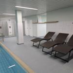 Innenpool mit Liegestühlen und Duschen im Hintergrund.