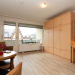 Zimmer mit Holzmöbeln, Balkon und TV. Arbeitsplatz mit Lampe.