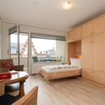 Zimmer mit Schlafgelegenheit, Schreibtisch und Balkonansicht