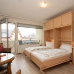 Zimmer mit zwei Betten, Schreibtisch und Balkon. Holzmöbel und Fernseher.