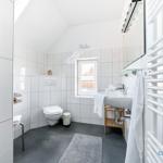 Badezimmer mit Toilette, Waschbecken und Heizung. Fenster und Spiegel sichtbar.