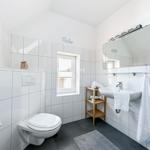 Badezimmer mit Toilette, Waschbecken und Dusche. Weiße Fliesen und dunkler Boden.