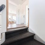 Treppe mit Teppichstufen führt in ein Wohnzimmer mit Esstisch und Stühlen.