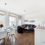 Wohn- und Essbereich mit Sofa, Tisch und Stühlen sowie Fenstern mit Blick nach draußen.