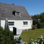 House with garden, parasol, and flower beds. Skylight and white facade.