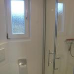 Shower area with glass enclosure, toilet paper holder, and small window with tinted glass.