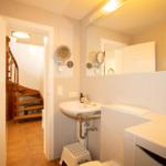 Bathroom with sink, mirror, and staircase in the background.
