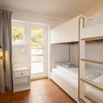 Room with bunk bed, window, and small cabinet.