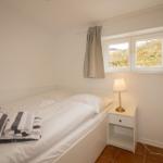 A bedroom with a bed, nightstand, and window. Folded towels are on the bed.