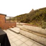 Terrace with table, benches, and view of green hills.