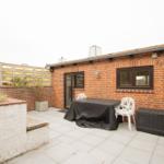 Terrace with table, chairs, and garden furniture beside red brick house