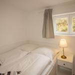 Bedroom with bed, nightstand, and lamp. Window with view of greenery.