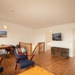 Living area with dining table, seating, and TV. Staircase to bedroom.