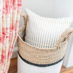 A basket with a pillow is next to a curtain.