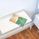 A book rests on a white bedside table next to a bed.