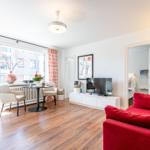 Living room with red sofa, TV and table with chairs. Passage to bedroom.