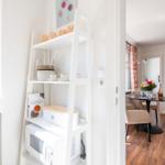 Kitchen area with microwave and shelf. View into living room with table and seating area.