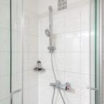 Shower with glass enclosure and chrome fixtures on white marble tiles