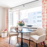 Dining table with two chairs in front of large window overlooking buildings.