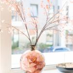 On the windowsill, there is a vase with cherry branches and a bowl.