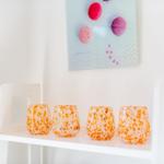 Four orange-speckled glasses sit on a white shelf.