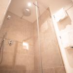 Dusche mit Duschbrause und Handbrause, Wandfliesen und Handtücher.