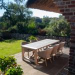 Terrasse mit Tisch und Stühlen, umgeben von Garten und Steinmauer.