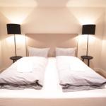 Doppelbett mit zwei Kissen und zwei Nachttischen mit Lampen.