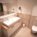 Badezimmer mit Waschbecken, Spiegel und Toilette. Fliesenwand und Boden.