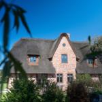 Haus mit strohgedecktem Dach und Backsteinfassade im Grünen.