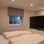 Schlafzimmer mit Bett, Fenster und Fernseher an der Wand.