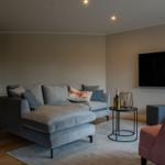 Wohnzimmer mit grauem Sofa, rotem Sessel und Wandfernseher.