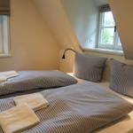 Schlafzimmer mit Doppelbett, zwei Fenstern und zwei Nachttischen mit Lampen.