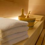 Sauna mit Holzbank, gefalteten weißen Handtüchern und Holzschale mit Löffeln.
