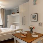 Schlafzimmer mit Bett, Tisch und Fenster. Auf dem Tisch stehen Tassen und Brot.