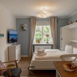 Schlafzimmer mit Bett, TV und Essplatz. Fenster mit Blick auf Grün.