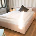 Schlafzimmer mit Bett, Nachttisch und Lampe. Holzboden und gestreifter Wandverkleidung.
