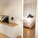 Schlafzimmer mit Bett und Streifenwand. Wohnbereich mit TV und Schrank.