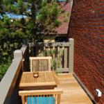 Terrasse mit Holztisch und Stühlen, roter Backsteinwand und grüner Umgebung.
