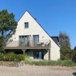 Moderne Villa mit Balkon und großem Fenster. Umgeben von Bäumen und Grünflächen.