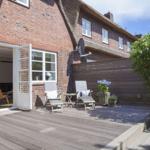 Terrasse mit Sitzgelegenheiten und Blick in das Haus. Holzdeck und Pflanzen sind sichtbar.