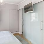 Schlafzimmer mit Bett, Fenster und Schlafzimmerwand. Fernseher an der Wand.