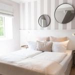 Schlafzimmer mit Bett, zwei Nachttischen und runden Spiegeln an gestreifter Wand.