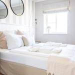 Schlafzimmer mit Bett, Kissen und Fenster. Zwei runde Spiegel an der Wand.