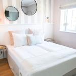 Schlafzimmer mit Bett, zwei runden Spiegeln und Fenster mit Lampen.