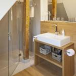 Badezimmer mit Dusche, Waschbecken und Toilette. Holz- und Glasgestaltung.