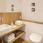 Badezimmer mit Waschbecken, Toilette und Holzregalen.