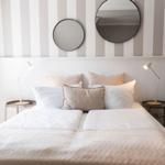 Schlafzimmer mit gestreifter Wand, zwei runden Spiegeln und einem Bett mit Kissen.