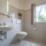 Badezimmer mit Waschbecken, Toilette und Fenster mit Vorhängen.