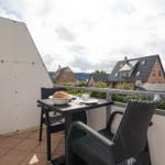 Terrasse mit Tisch und Stühlen, Blick auf Wohnhäuser und Grünflächen.